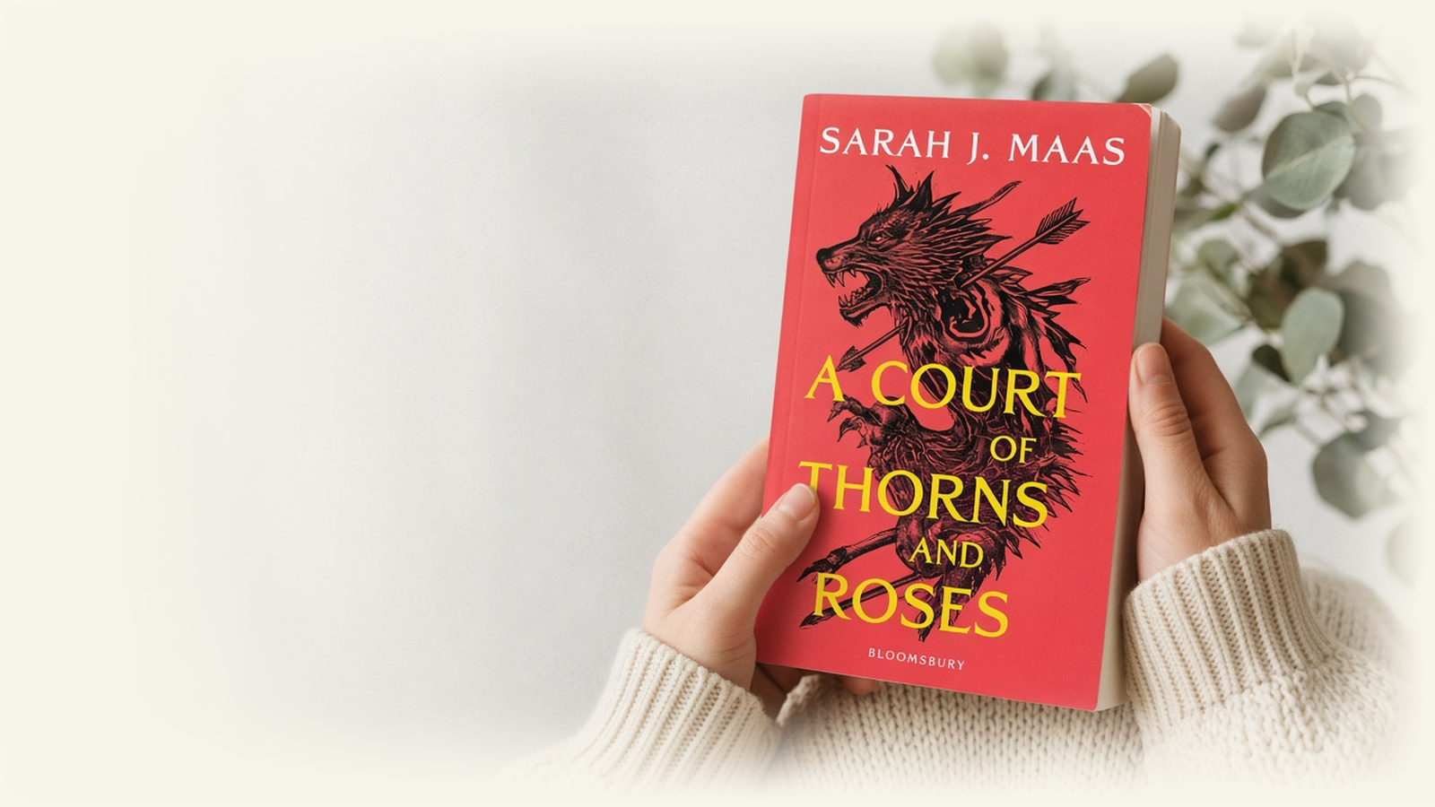 Hands holding A Court of Thorns and Roses by Sarah J. Maas, Bloomsbury red-beast cover.